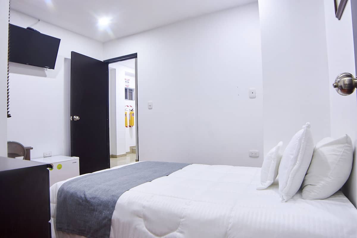Ein Schlafzimmer mit Bett, Schreibtisch, Stuhl, Fernseher und einer Tür zu einem anderen Raum.