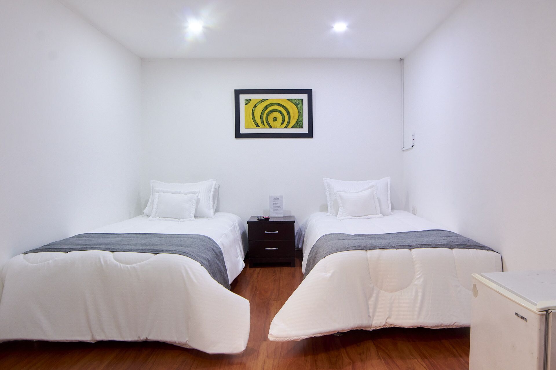 A small, clean room with two beds, a nightstand, and a wall-mounted artwork.