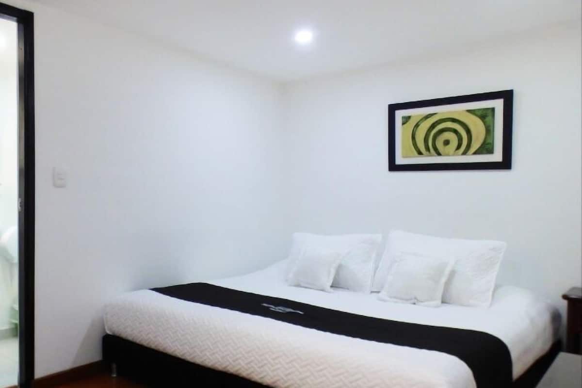 Ein Schlafzimmer mit einem Bett, weißen Wänden, einem schwarzen Kopfteil und einem gerahmten Kunstwerk an der Wand.
