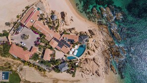 Luftaufnahme eines Küsteneigentums mit Swimmingpool, mehreren Zimmern und einem Strandabschnitt.