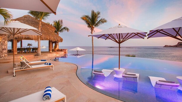 Piscina infinita con sillones de descanso y sombrillas, con vista al mar.