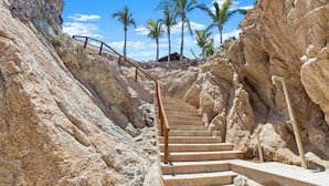 Una escalera que asciende por una ladera rocosa, con palmeras al fondo.