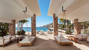 Un área de descanso frente a la playa con camas colgantes, una piscina y vistas al mar.