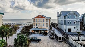 En ejendom ved stranden med et toetagers hus, en overdækket veranda og udsigt over stranden.