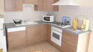 Eine kleine Küche mit Holzschränken, einer Mikrowelle, einem Gasherd und einer Kaffeemaschine.