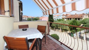 Un balcón con una mesa y sillas, un toldo a rayas y vistas a casas vecinas.