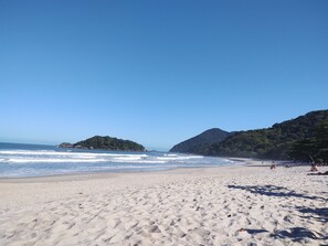 A beach with a clear sky, calm sea, and distant mountains.