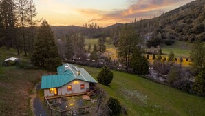 Una casa amb teulada verda, envoltada per un turó forestal.