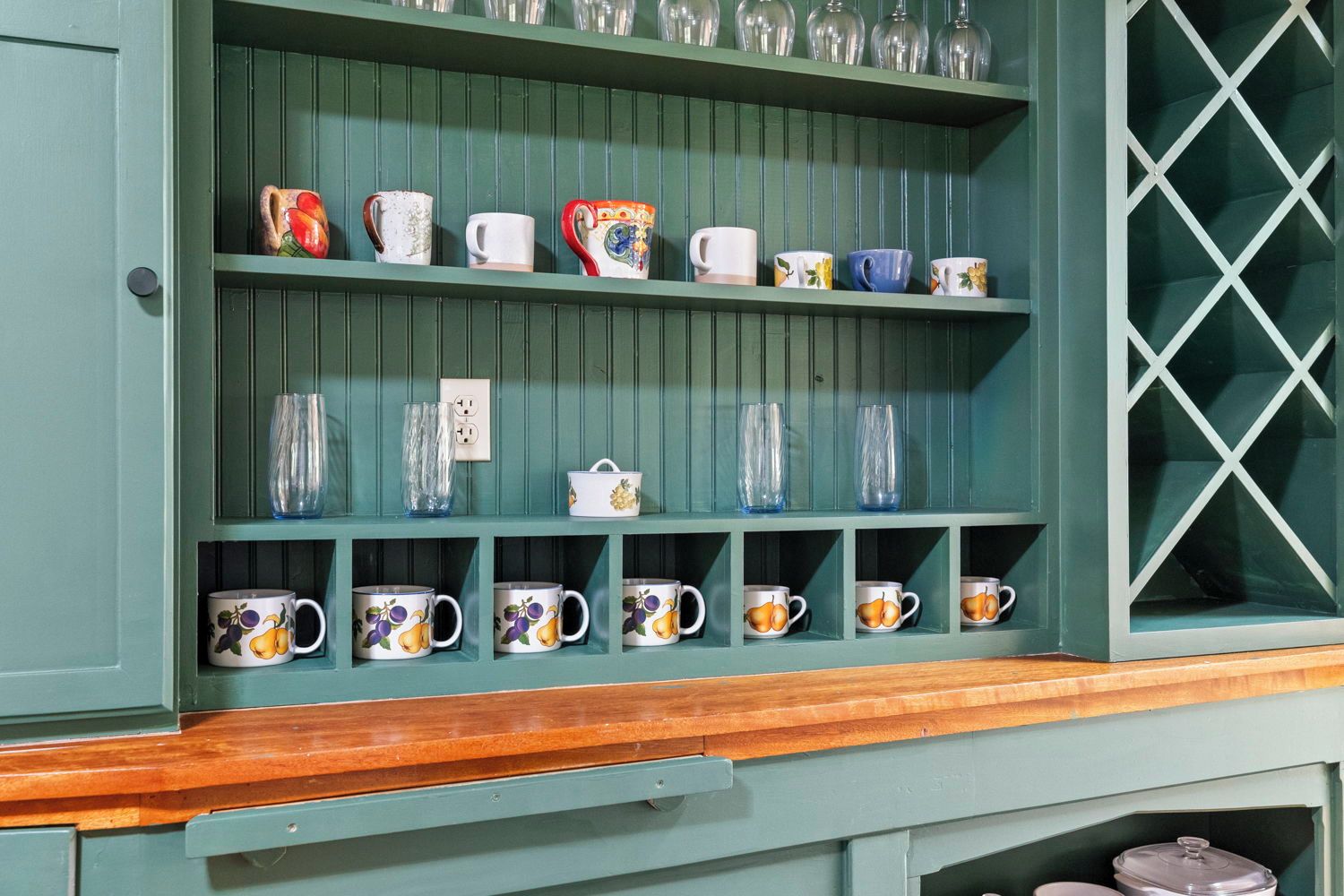 A green wooden shelf with various glassware and ceramic mugs.