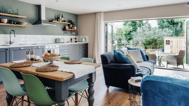 Una cocina moderna con estantes de madera, una mesa de comedor con sillas y vista al exterior.