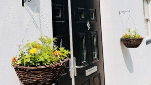 A black door with a sign above it reading "Higher Lane House." There are two hanging baskets with plants on either side of the door. - Higher Lane House (Plymouth)