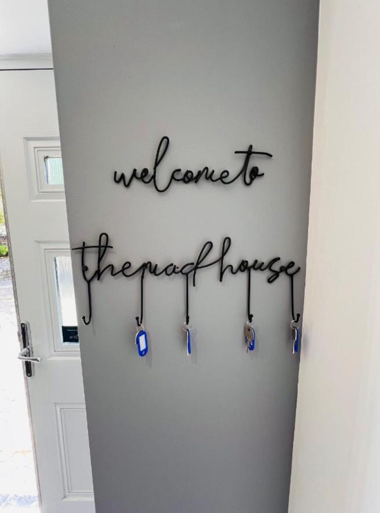 Un letrero en la pared con el texto 'welcome to the past house' y un juego de llaves colgando debajo.