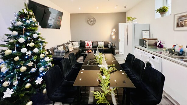A modern kitchen with a dining area, a Christmas tree, and a flat-screen TV mounted on the wall. - Higher Lane House (Plymouth)