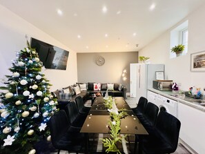 A modern kitchen with a dining area, a Christmas tree, and a flat-screen TV mounted on the wall. - Higher Lane House (Plymouth)
