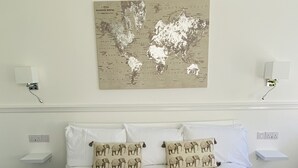A neatly made bed with white linens and two elephant-patterned pillows, a world map on the wall, and a bedside table with a book and toiletries. - Higher Lane House (Plymouth)