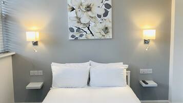 A neatly made bed with white linens, two bedside tables with lamps, a wall-mounted artwork of flowers, and a black textured rug.
