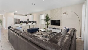 A modern living room with a brown leather sofa, a glass coffee table, and a flat-screen TV mounted on the wall. - 8 Bedroom Home inside the best resort in Orlando, GOLF VIEW! (Four Corners)