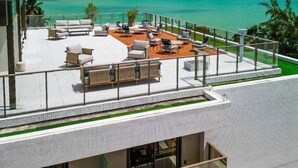 A rooftop terrace with outdoor seating, overlooking a turquoise sea and clear sky.