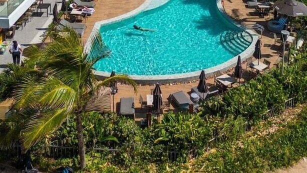 A resort with a large, winding pool surrounded by palm trees and a beach.