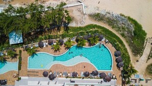 An aerial view of a resort with a large swimming pool, beach, and lounge area.