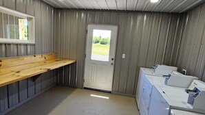 Pesuhuone, jossa on puinen penkki, ovi, josta on näkymä, ja päällekkäin sijoitettuja pesukoneita.