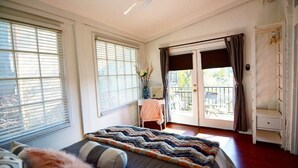 Quarto com cama, escrivaninha e varanda.