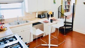Cozinha compacta com armários brancos, fogão a gás e pequena área de refeições com cadeiras brancas.