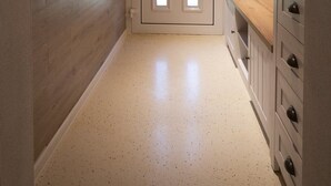Un couloir étroit doté d’un plancher en bois, une porte blanche avec une fenêtre triangulaire et un meuble en bois avec des tiroirs.