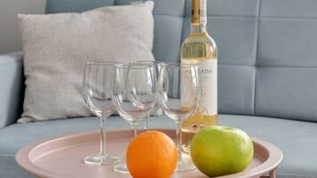 A pink tray with a bottle of wine, two fruits, and empty glasses on a sofa.