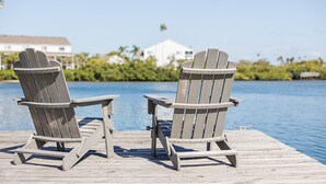 Two Adirondack chairs on a wooden dock by a body of water with buildings and greenery in the background. - Waterfront Home 3 Blocks to the Beach! (Indian Rocks Beach)