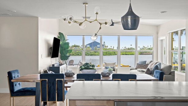 A modern kitchen with a large island, dining area with blue chairs, and a view of the water. - Waterfront Home 3 Blocks to the Beach! (Indian Rocks Beach)