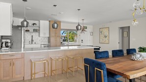 A modern kitchen with a central island, bar stools, and a dining table with blue upholstered chairs. - Waterfront Home 3 Blocks to the Beach! (Indian Rocks Beach)