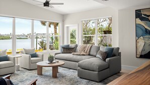 A modern living room with a grey sectional sofa, two armchairs, a coffee table, and large windows offering a view of the water. - Waterfront Home 3 Blocks to the Beach! (Indian Rocks Beach)