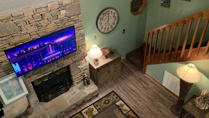 A cozy living room with a stone fireplace, a flat-screen TV, a clock, and a staircase. -  2 minutes to Parkway, 5 minutes to The Island & Dollywood!  (Pigeon Forge)