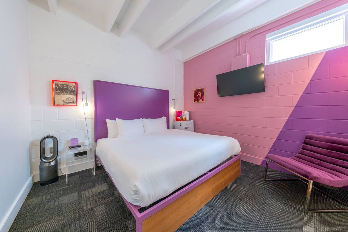 A bedroom with a bed, a nightstand, a chair, a TV, and a window.