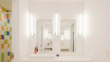 Un baño con un lavamanos blanco, dos espejos y una zona de ducha con azulejos de colores.