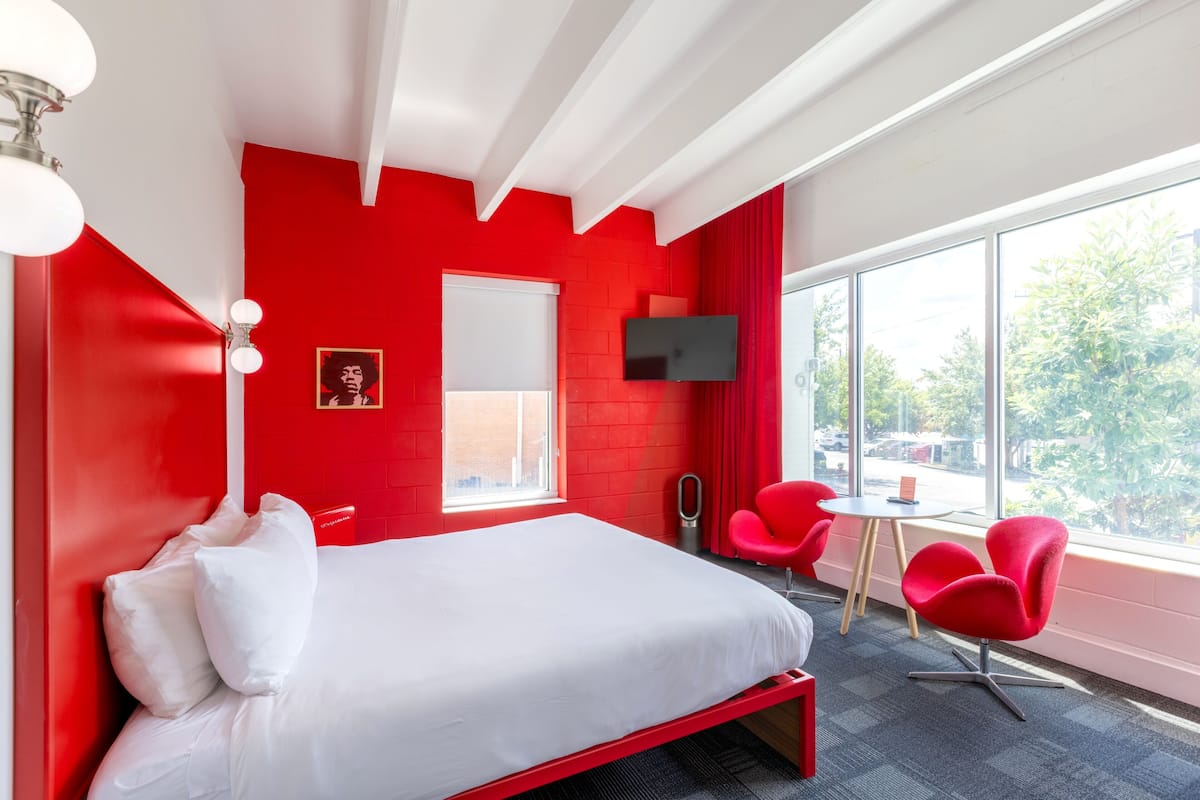A red-walled room with a bed, a TV, a window, and red chairs.