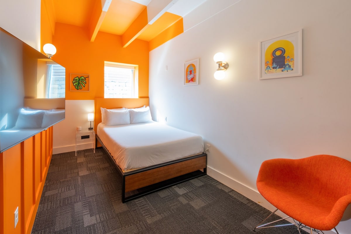A hotel room with a bed, a desk, a chair, and artwork on the walls.