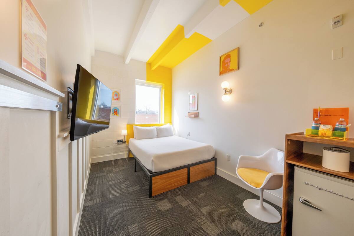 A hotel room with a bed, a TV, a desk with a chair, and a window.