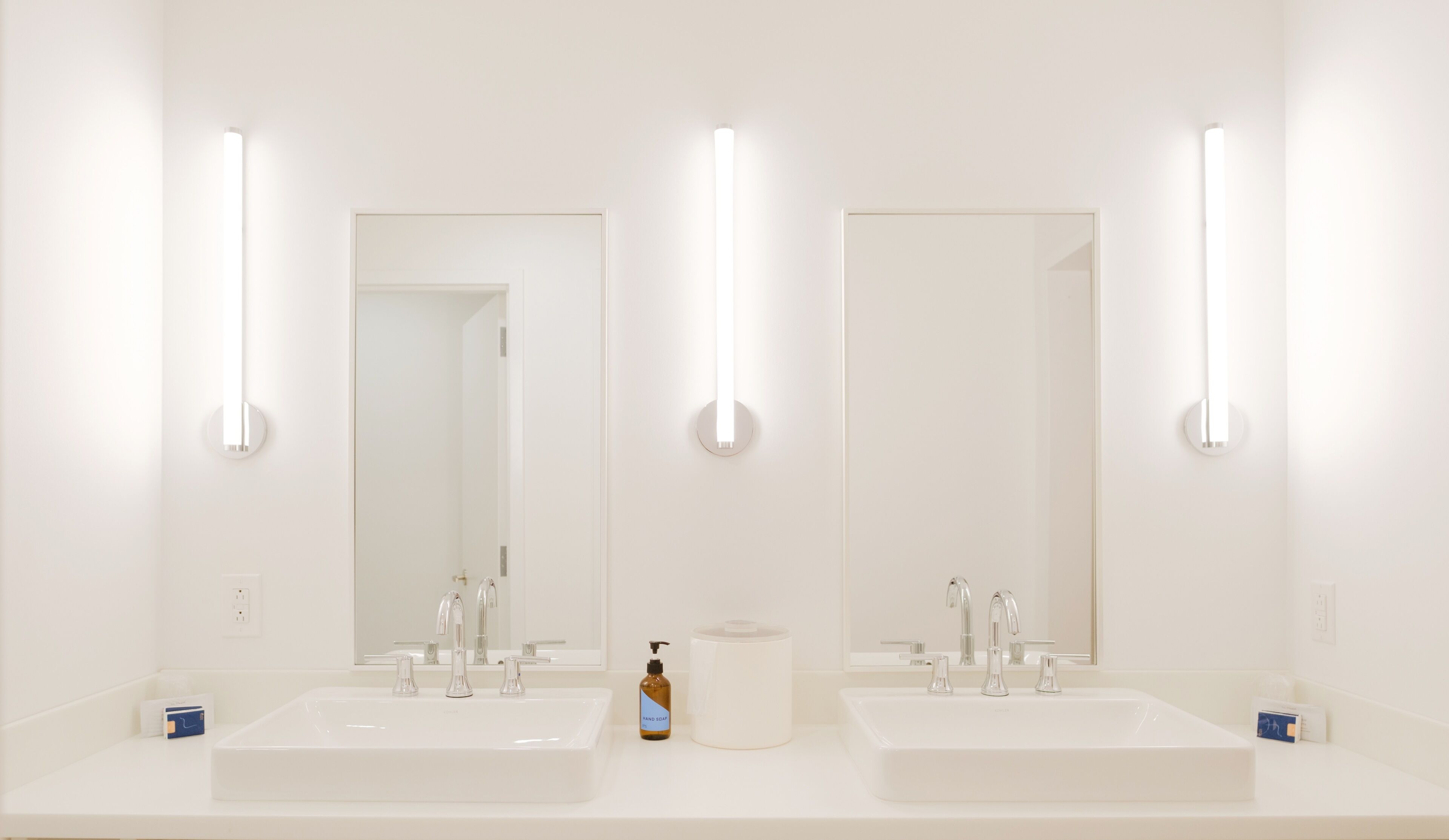 Une salle de bain avec deux lavabos, un miroir et un distributeur de savon liquide.