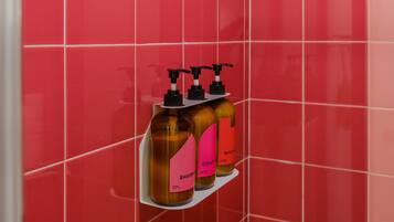 A bathroom with red tiles, a showerhead, and three bottles of body wash on a shelf.