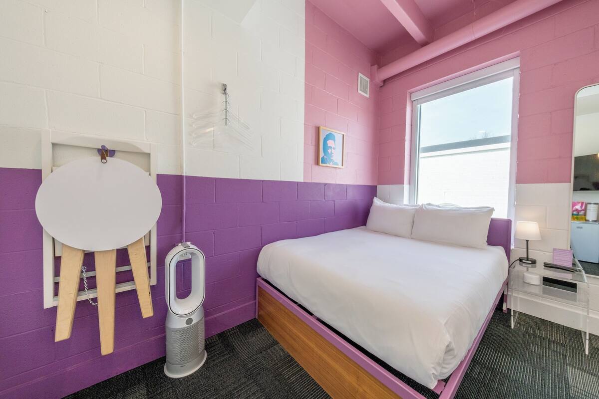 A room with a bed, a whiteboard, a picture on the wall, and a window.
