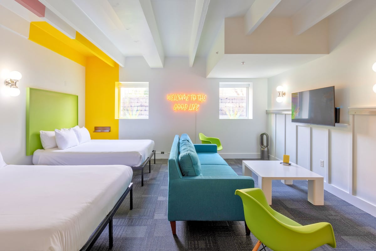 A hotel room with two beds, a sofa, a table, and a TV.