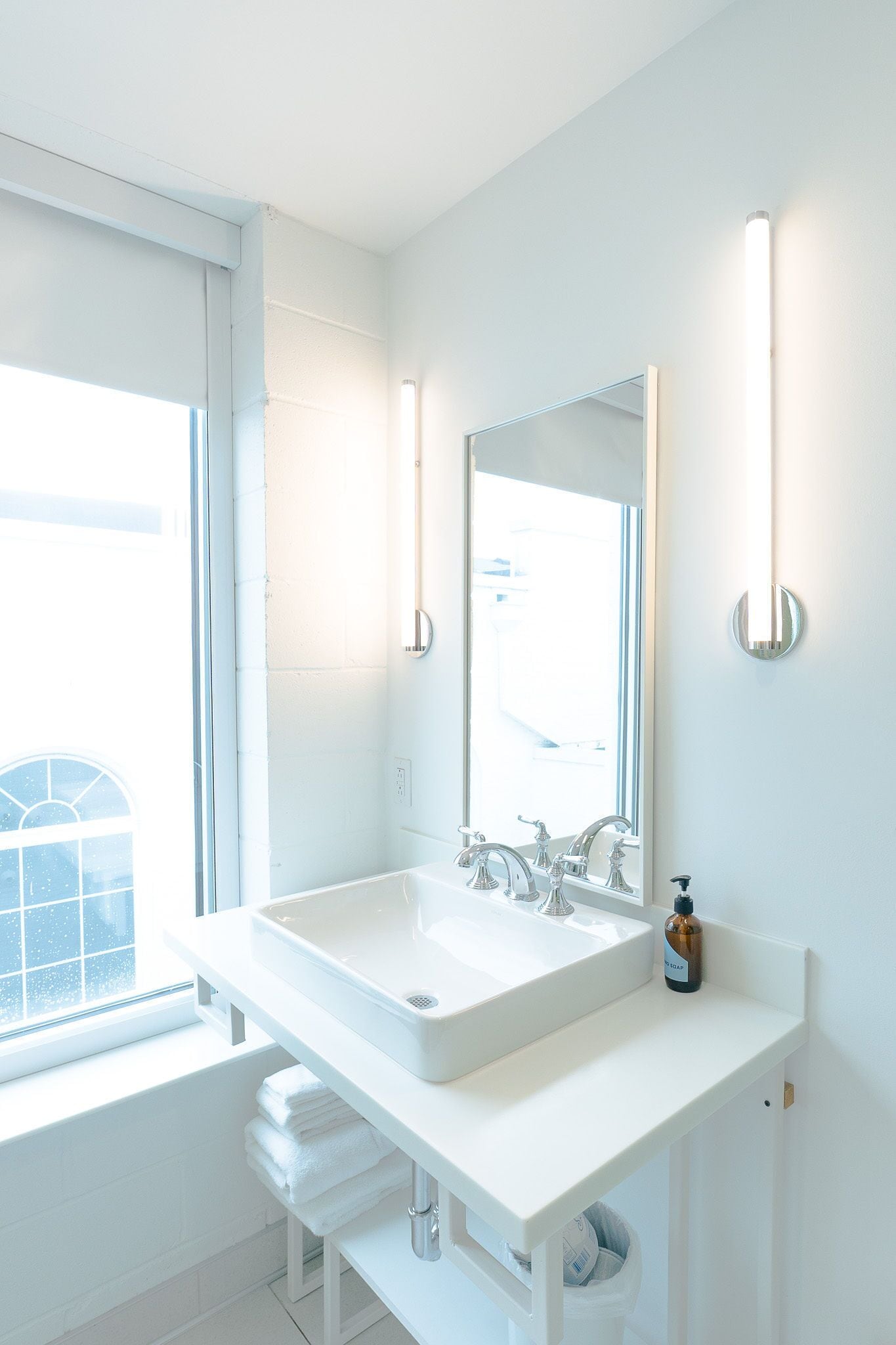 Un baño moderno con un lavabo blanco grande, un espejo y dos lámparas fijadas a la pared.