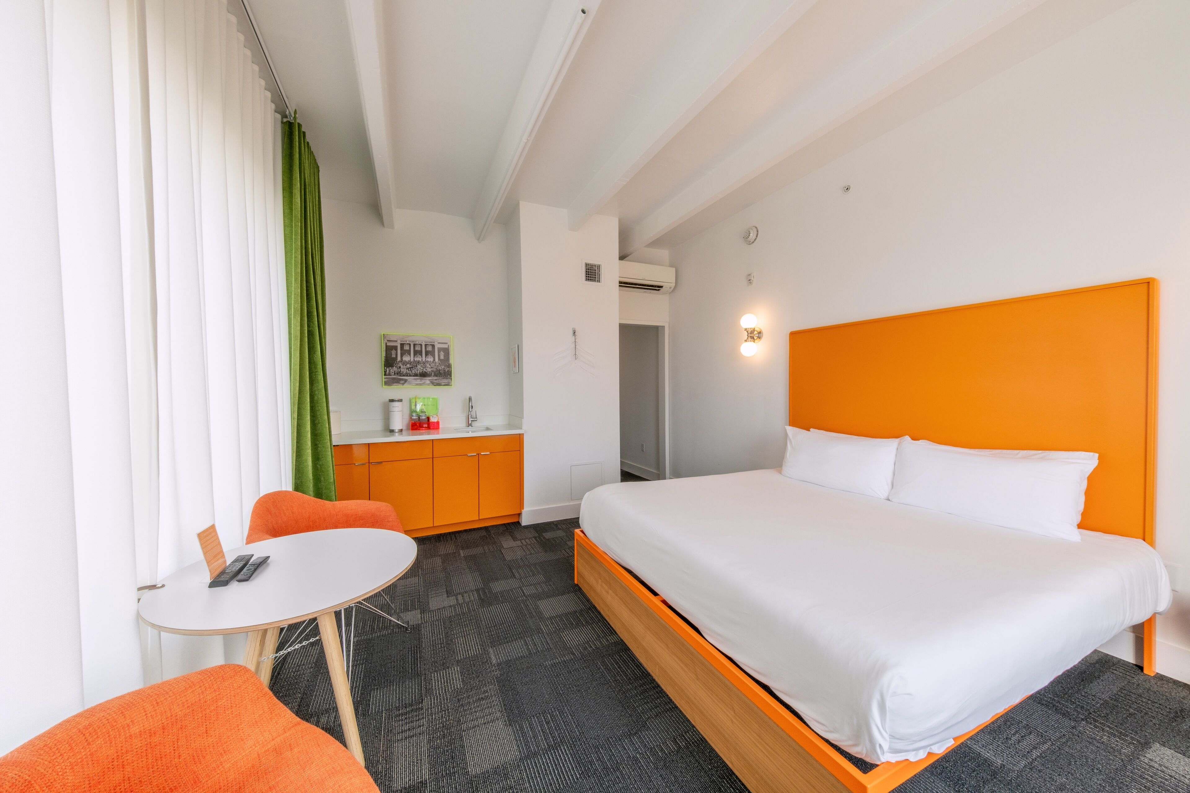 A hotel room with a bed, a small table, a chair, a desk, and a kitchenette.