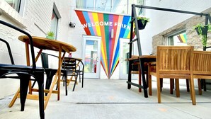 An outdoor seating area with tables and chairs, a 'WELCOME FRIEND' sign, and a building with large windows.