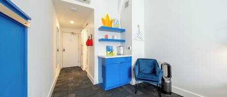 Un pasillo con una puerta azul, un armario azul con estantes, una silla azul y un bote de basura.