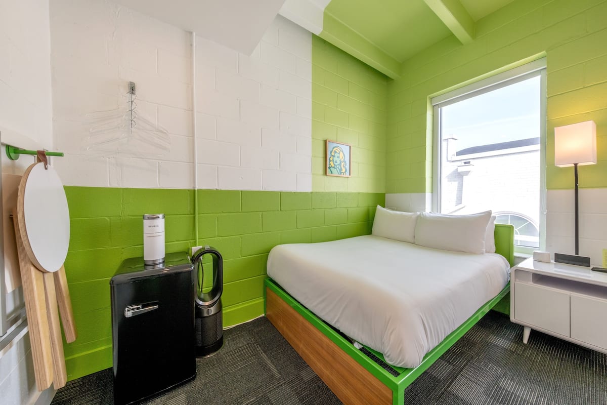 A room with a bed, a small kitchenette, a window, and a wall-mounted picture.