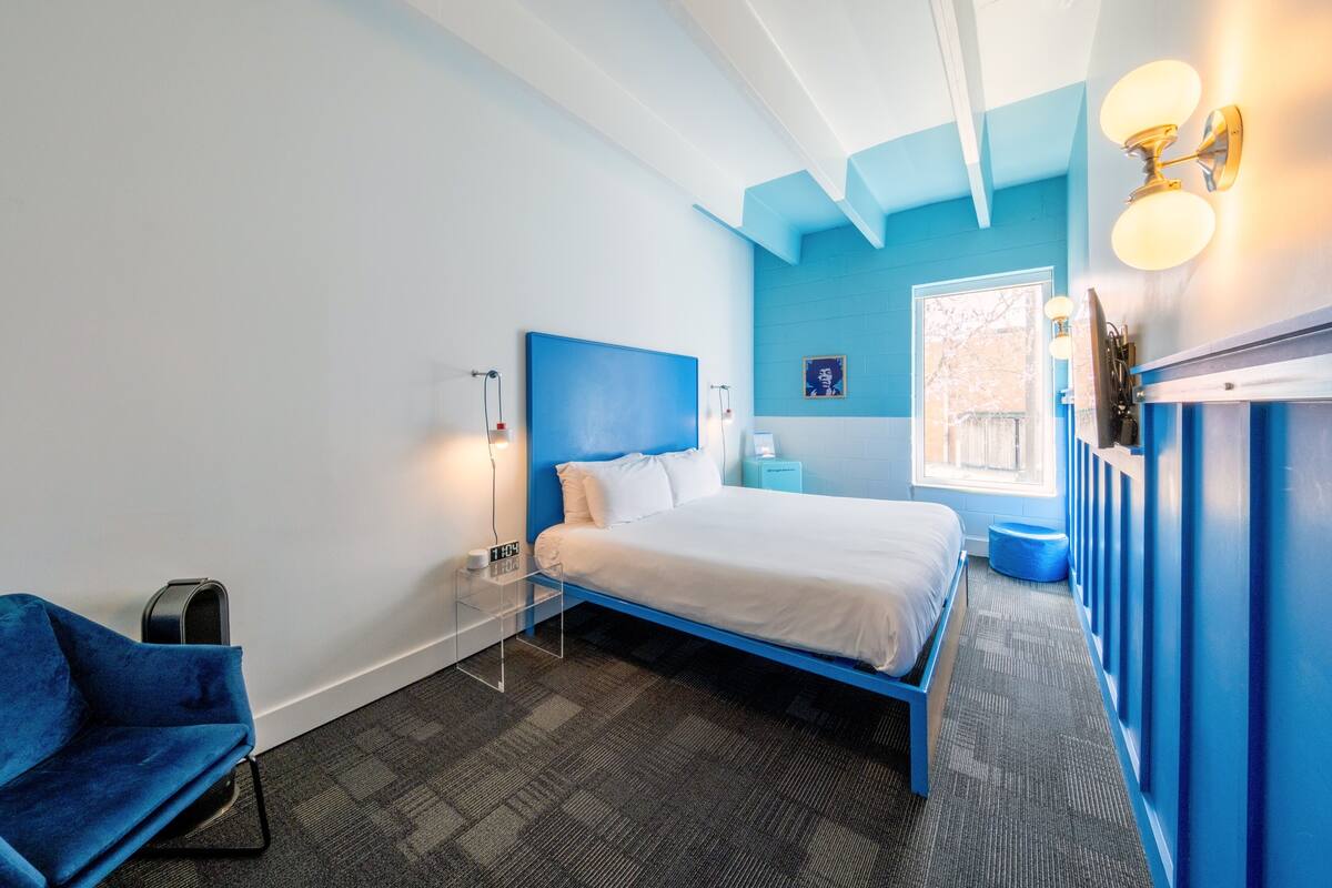A modern bedroom with a bed, bedside tables, a nightstand, a chair, and a window.