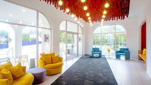 A modern interior with large windows, a yellow sofa, blue chairs, and a unique red hanging light fixture.